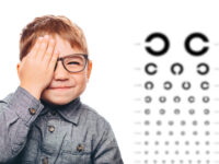 boy having eye exam with eye chart and covering one eye.